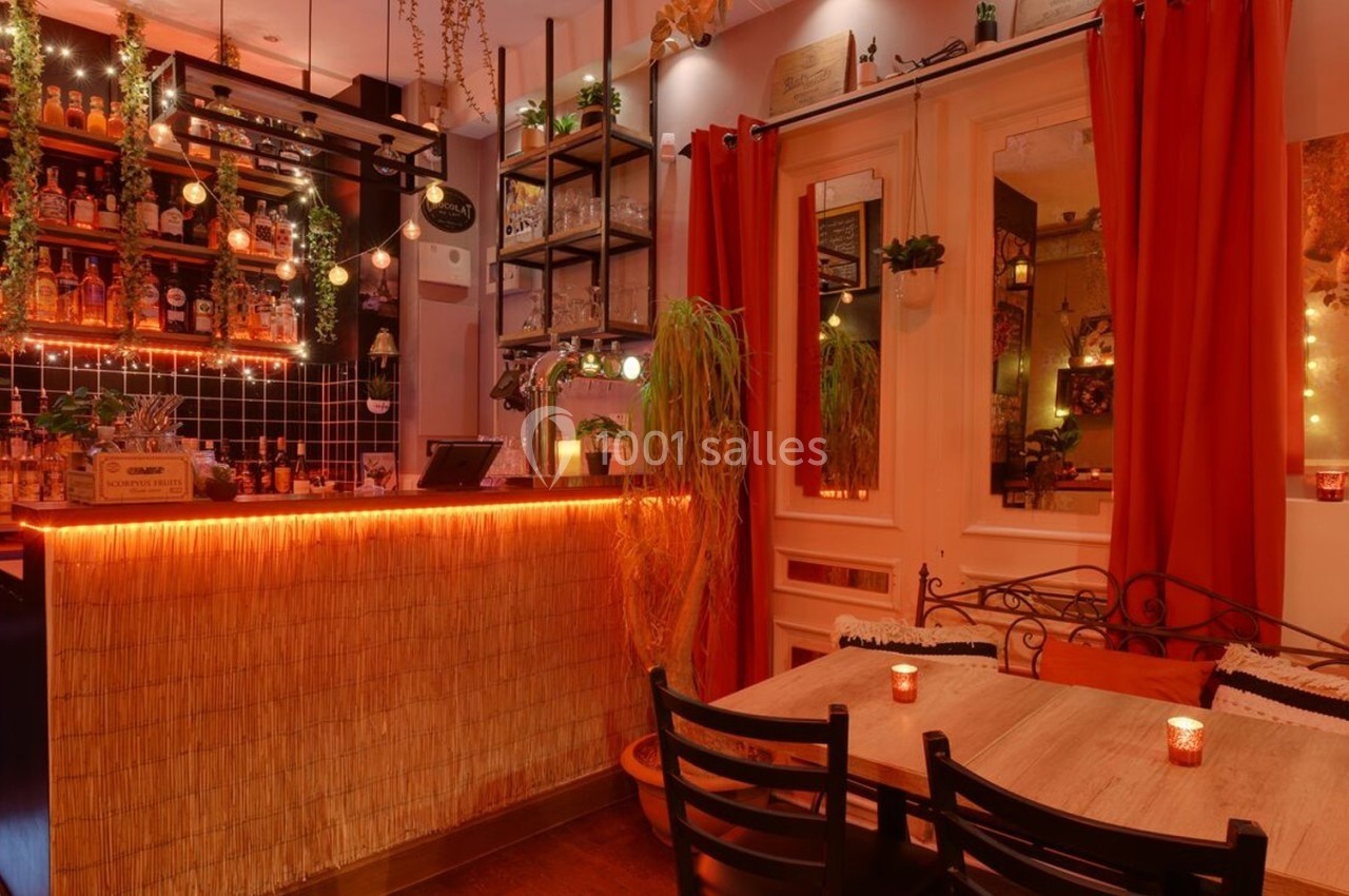 Intérieur d'un bar chaleureux avec un comptoir éclairé, des étagères de bouteilles et des tables en bois décorées de bougies.