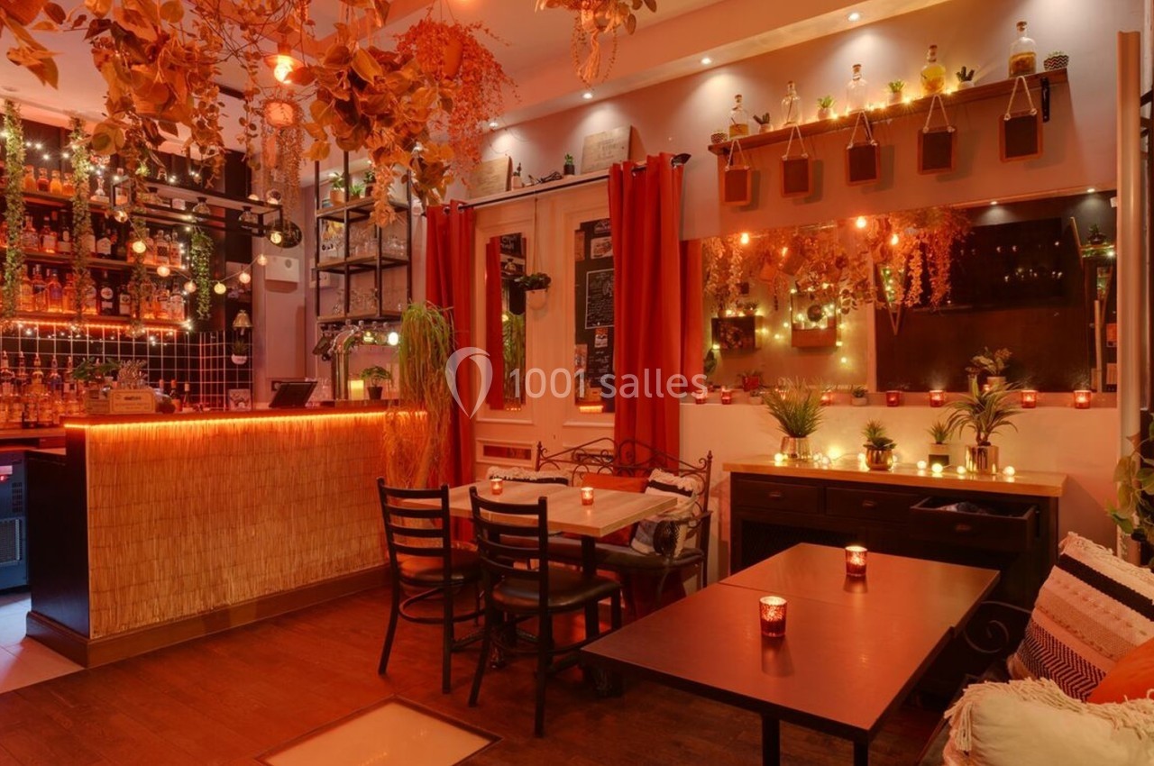 Salle de restaurant chaleureuse avec décoration végétale, éclairage tamisé et bougies sur les tables.