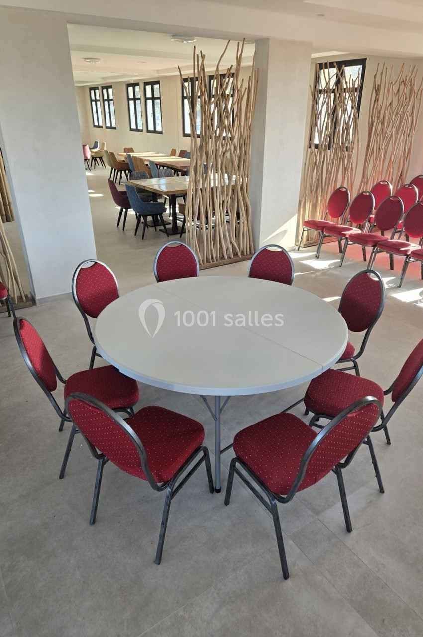 Salle lumineuse avec une table ronde blanche entourée de chaises rouges, et des séparateurs en bois en arrière-plan.