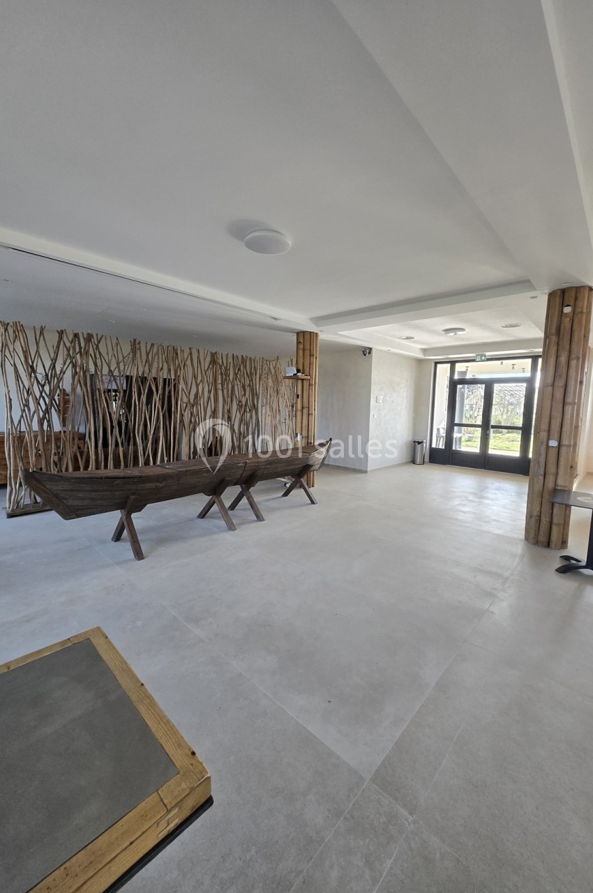 Espace intérieur lumineux avec sol en carrelage clair, banc en bois sculpté et cloison décorative en branches.
