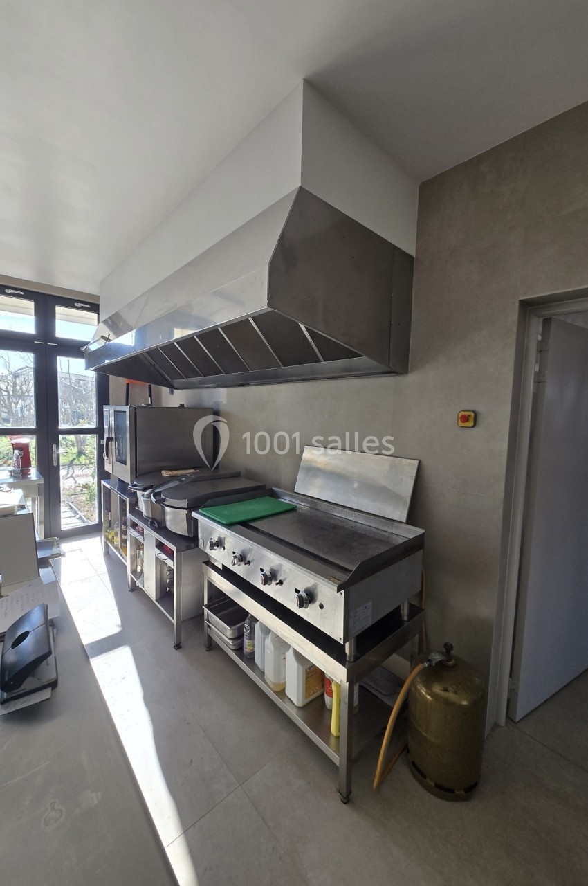 Cuisine professionnelle équipée d'une hotte en inox, de plaques de cuisson et de plans de travail en acier inoxydable.