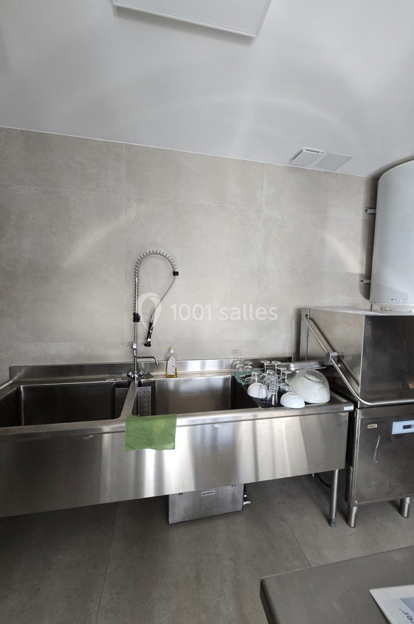 Évier professionnel en inox avec robinet flexible, vaisselle propre et lave-vaisselle dans une cuisine sobre.