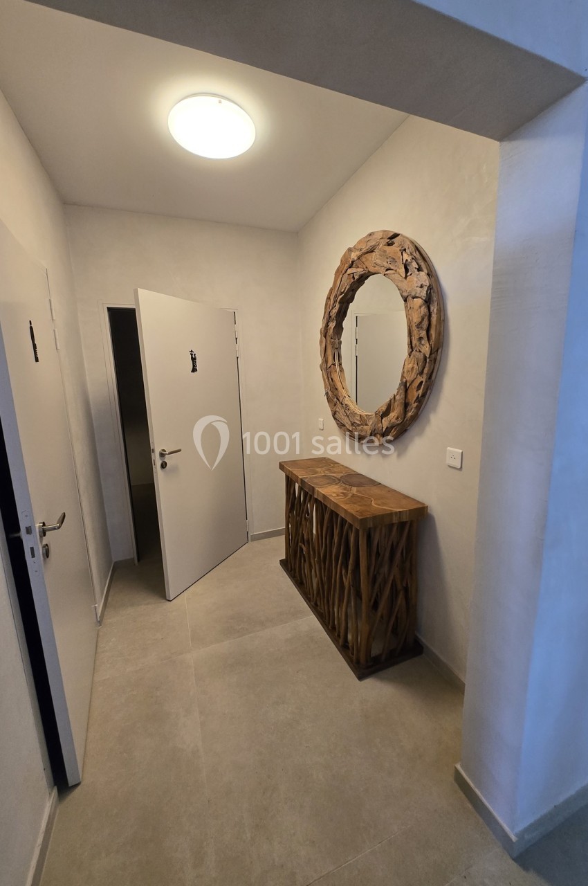 Entrée avec un meuble en bois sculpté, un miroir rond encadré de bois et des portes blanches.