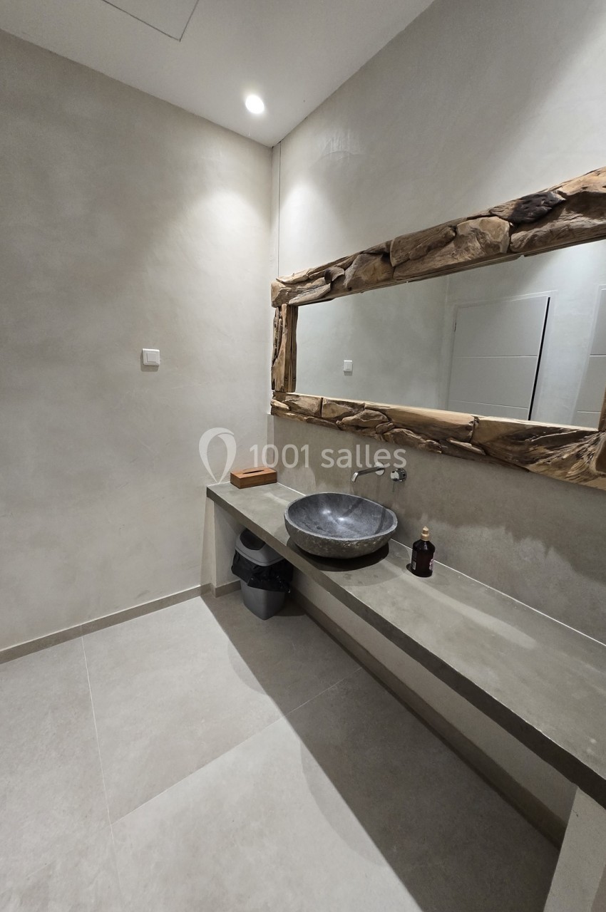 Salle de bain moderne avec lavabo en pierre, miroir encadré de bois brut et murs en béton ciré.