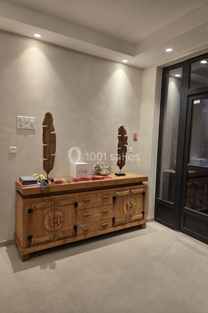 Buffet en bois avec décorations, situé dans un hall d'entrée moderne éclairé par des spots au plafond.