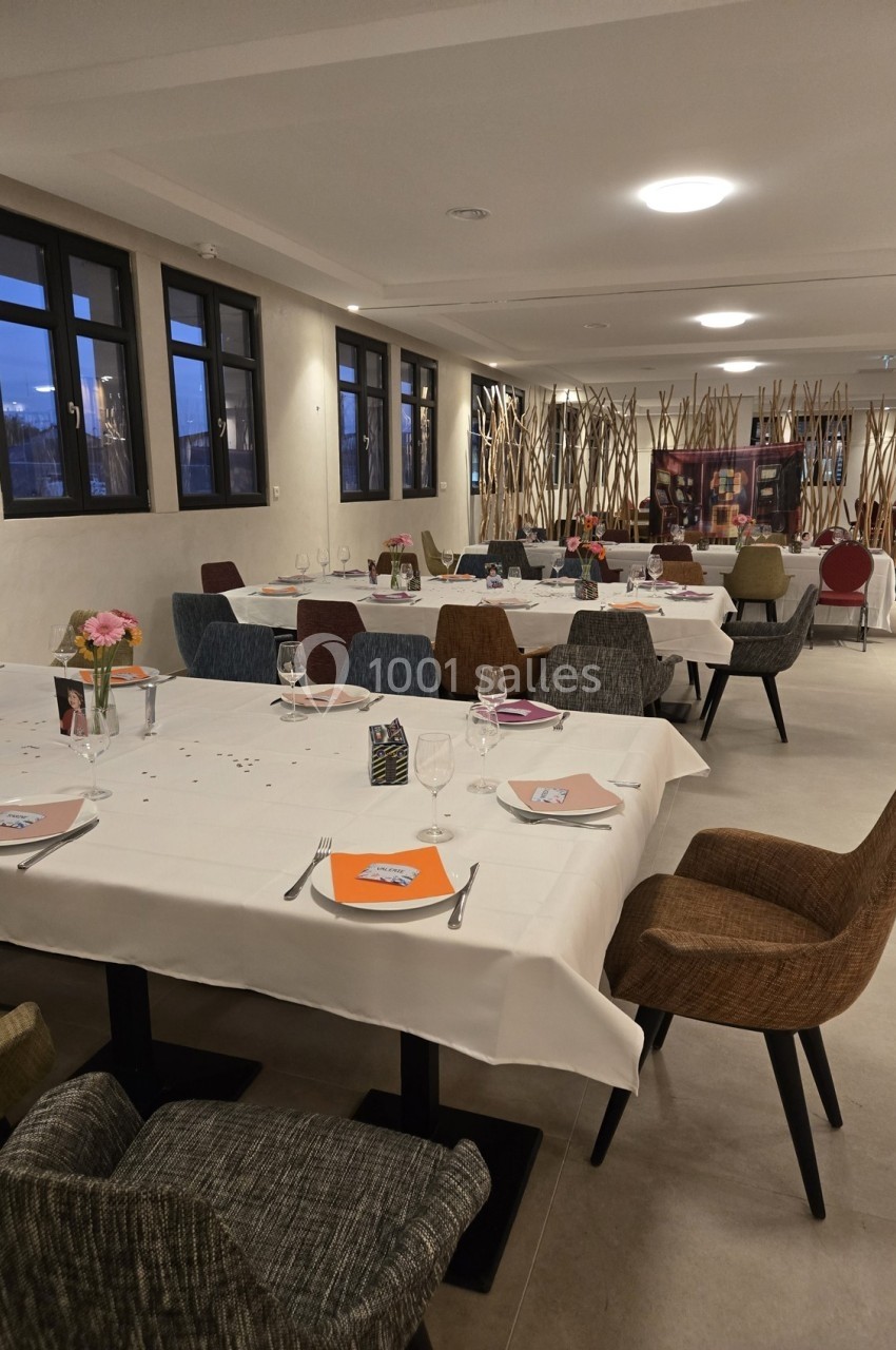 Salle de restaurant moderne avec tables dressées, chaises variées et grandes fenêtres laissant entrer la lumière naturelle.
