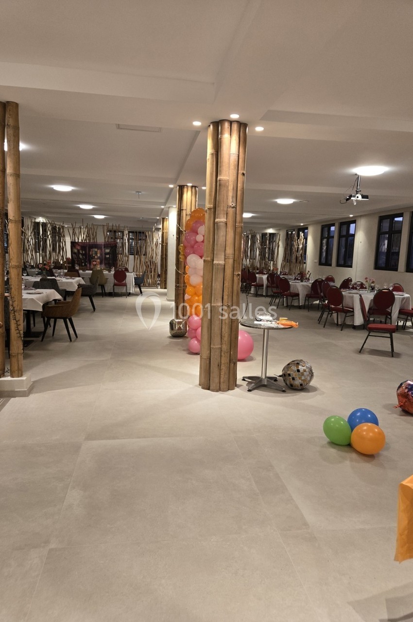 Salle de réception décorée avec des ballons colorés, des tables dressées et des colonnes en bambou.