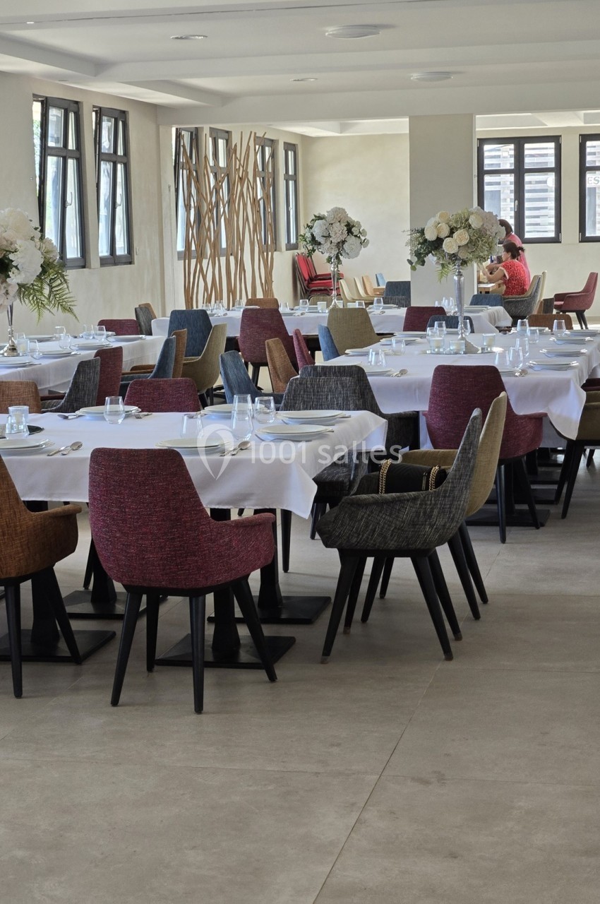 Salle de restaurant lumineuse avec des tables dressées, des chaises colorées et des compositions florales.