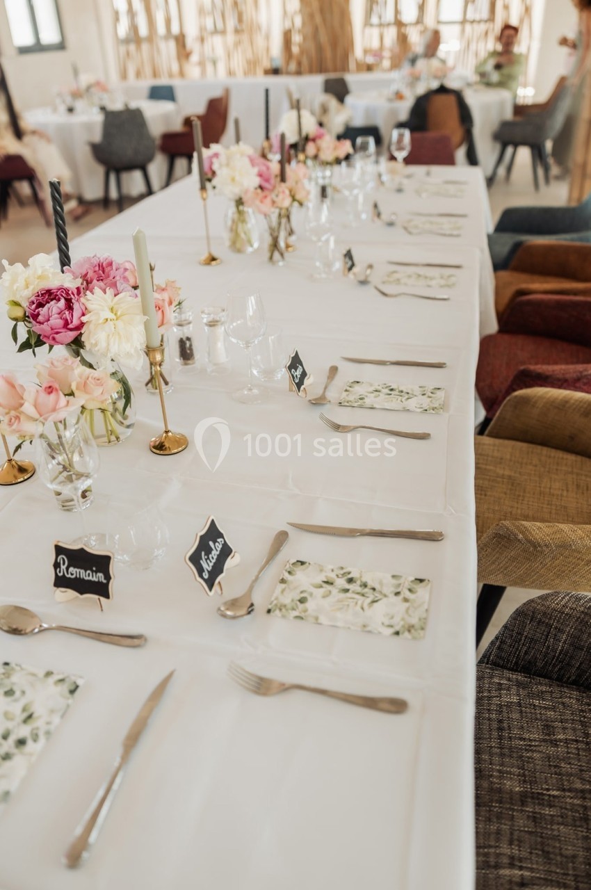 Table de réception élégamment dressée avec des fleurs, bougies et marque-places, entourée de chaises variées.