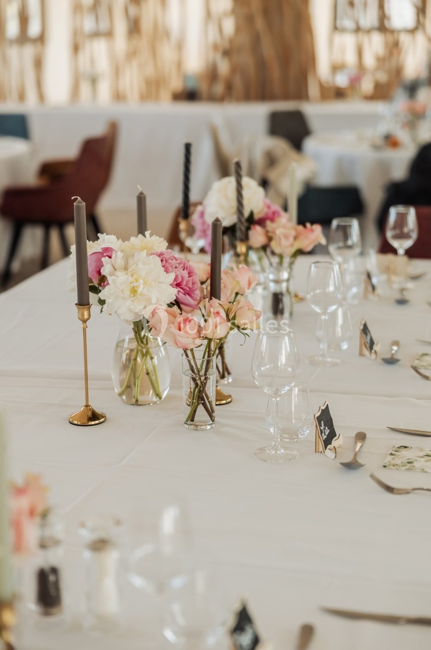 Table décorée avec des bougies, des vases de fleurs pastel et des verres, dans un cadre élégant et lumineux.