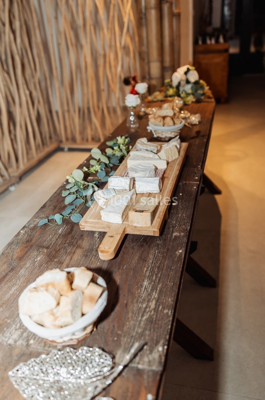 Plateau de fromages variés sur une table en bois, accompagné de pain et décoré de feuillage et fleurs.