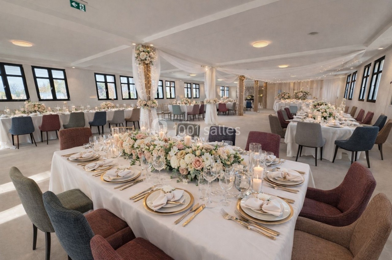 Salle de réception décorée pour un mariage, avec tables dressées, fleurs et éclairage chaleureux.