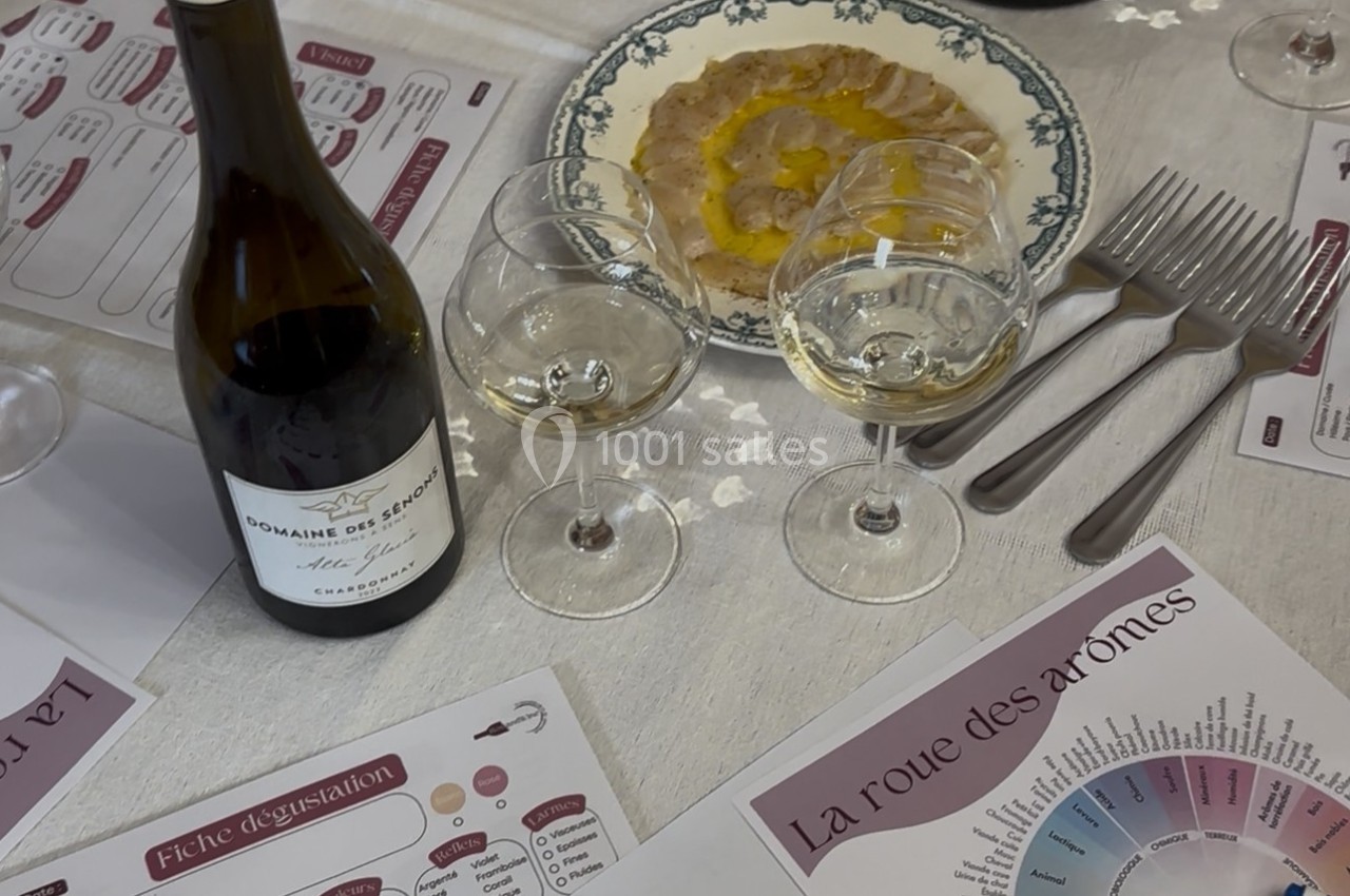 Bouteille de vin, verres remplis, assiette de carpaccio et documents de dégustation sur une table dressée.