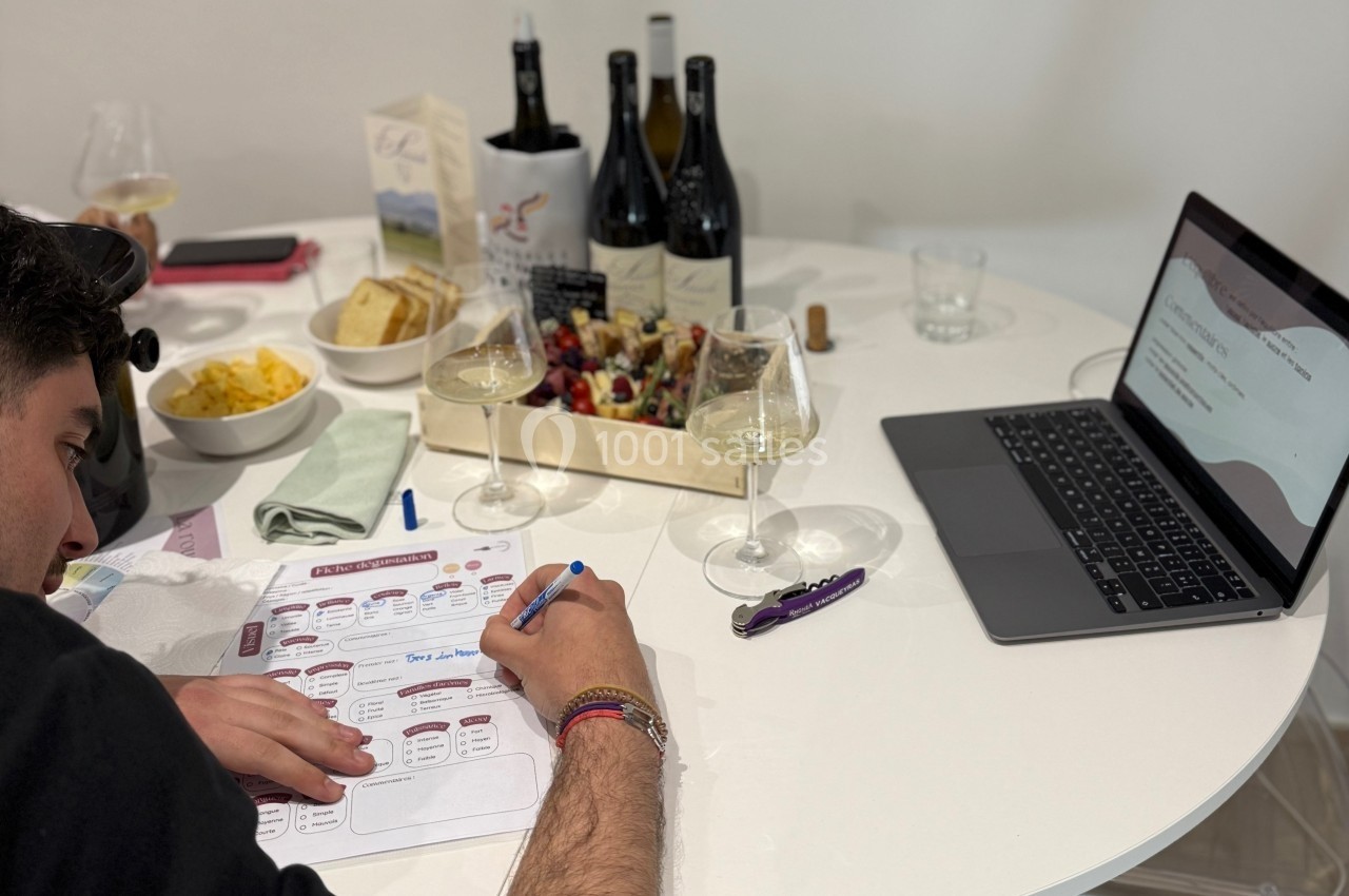 Un homme remplit un document sur une table avec des verres de vin, des bouteilles et un plateau de charcuterie.