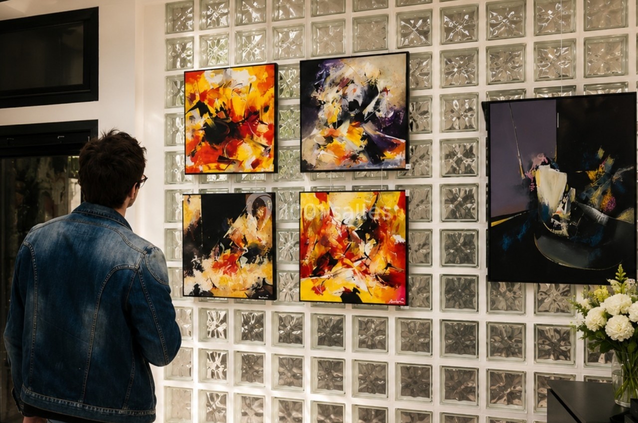 Un homme observe des tableaux abstraits colorés accrochés sur un mur en briques de verre dans une galerie d'art.