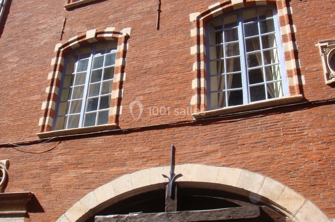 Façade en briques rouges avec fenêtres à encadrement clair et arc en pierre au-dessus d'une porte en bois.