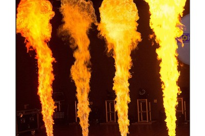 Jets de flammes verticales de différentes intensités émanant de dispositifs au sol dans une salle sombre.