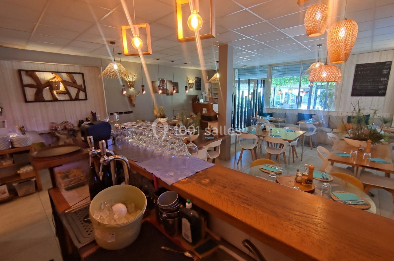 Salle de restaurant lumineuse avec tables dressées, décor chaleureux et vue sur l'extérieur à travers une baie vitrée.