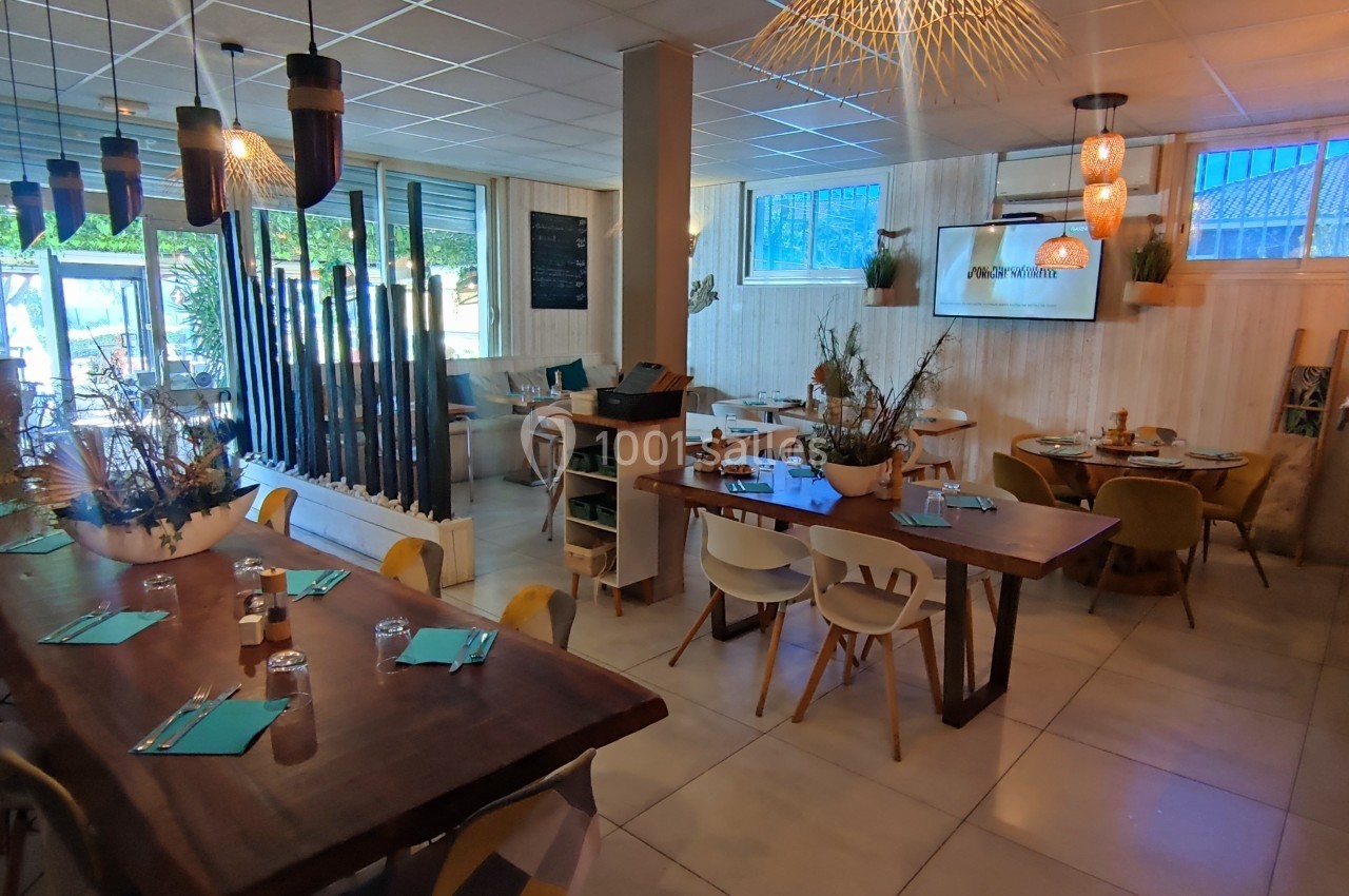 Salle de restaurant lumineuse avec tables en bois, décorations végétales et éclairage suspendu moderne.