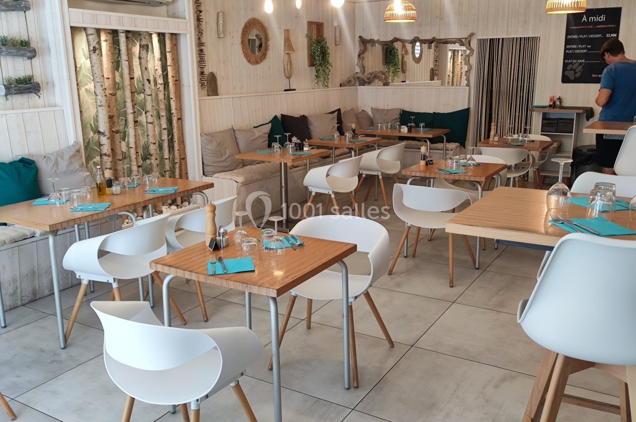 Salle de restaurant lumineuse avec tables en bois, chaises blanches et décoration naturelle aux tons clairs.