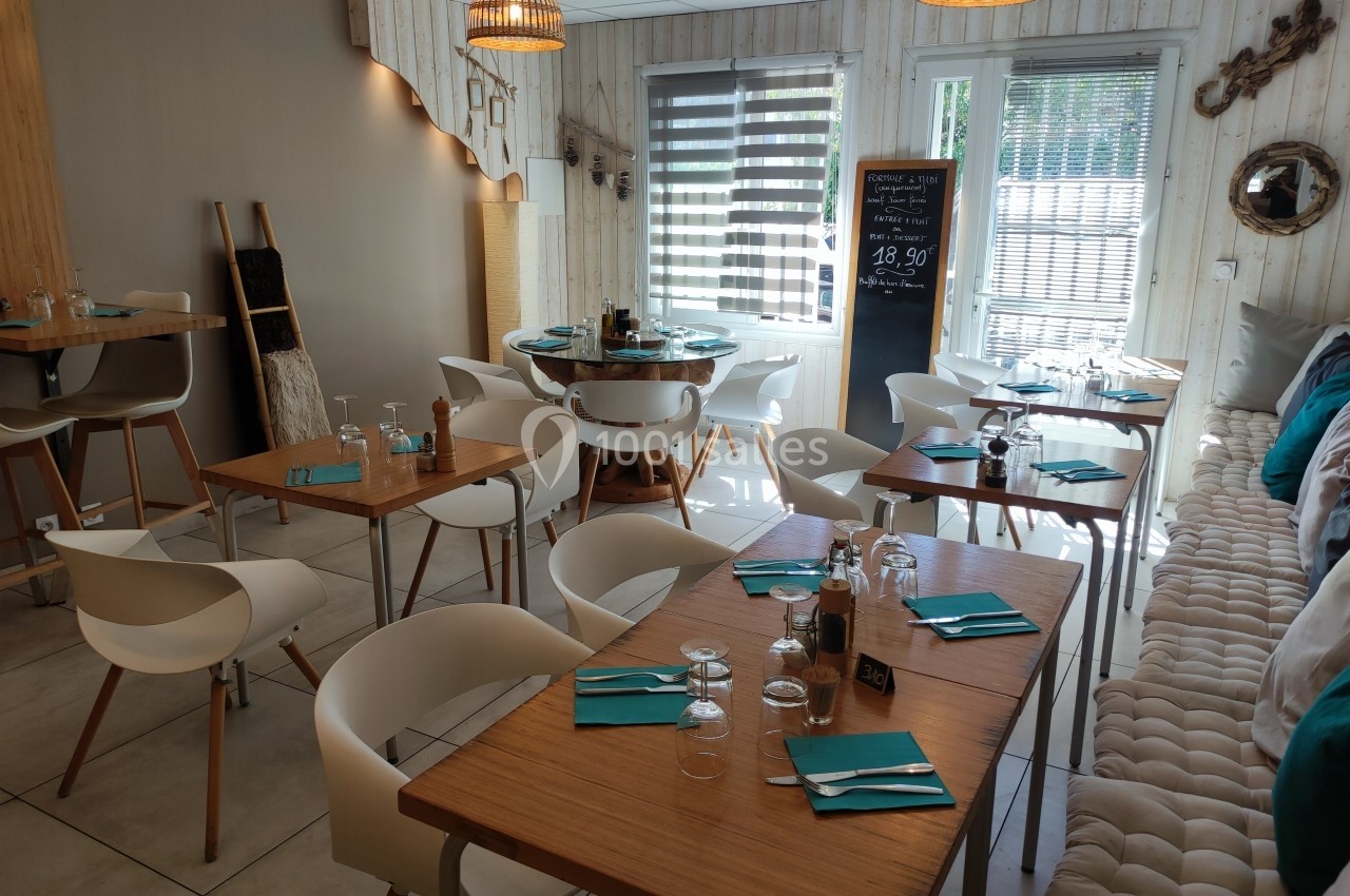Salle de restaurant lumineuse avec tables en bois, chaises blanches et décoration moderne.