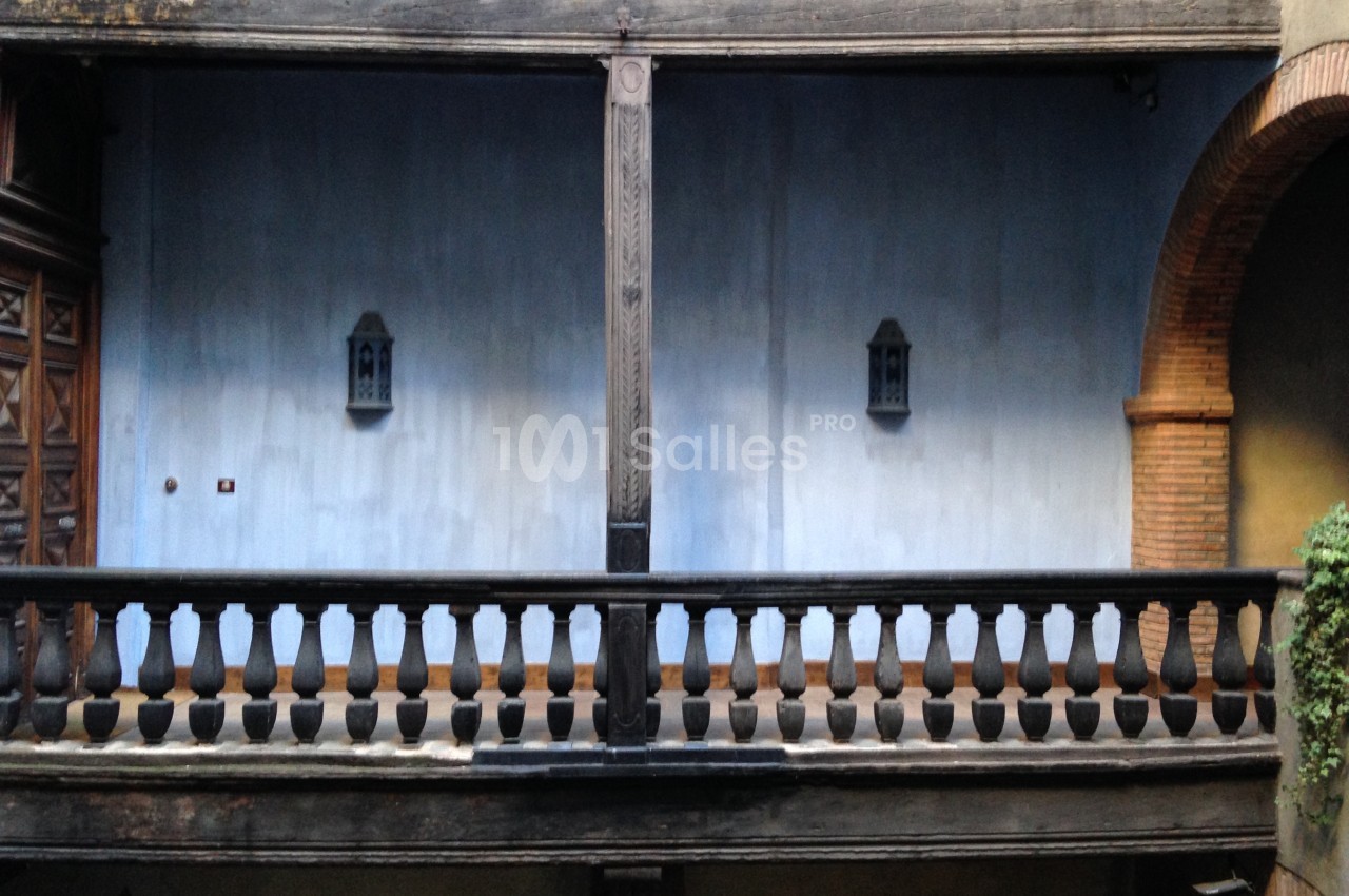 Balustrade en bois sombre devant un mur bleu avec deux lanternes, encadrée par des éléments en briques.