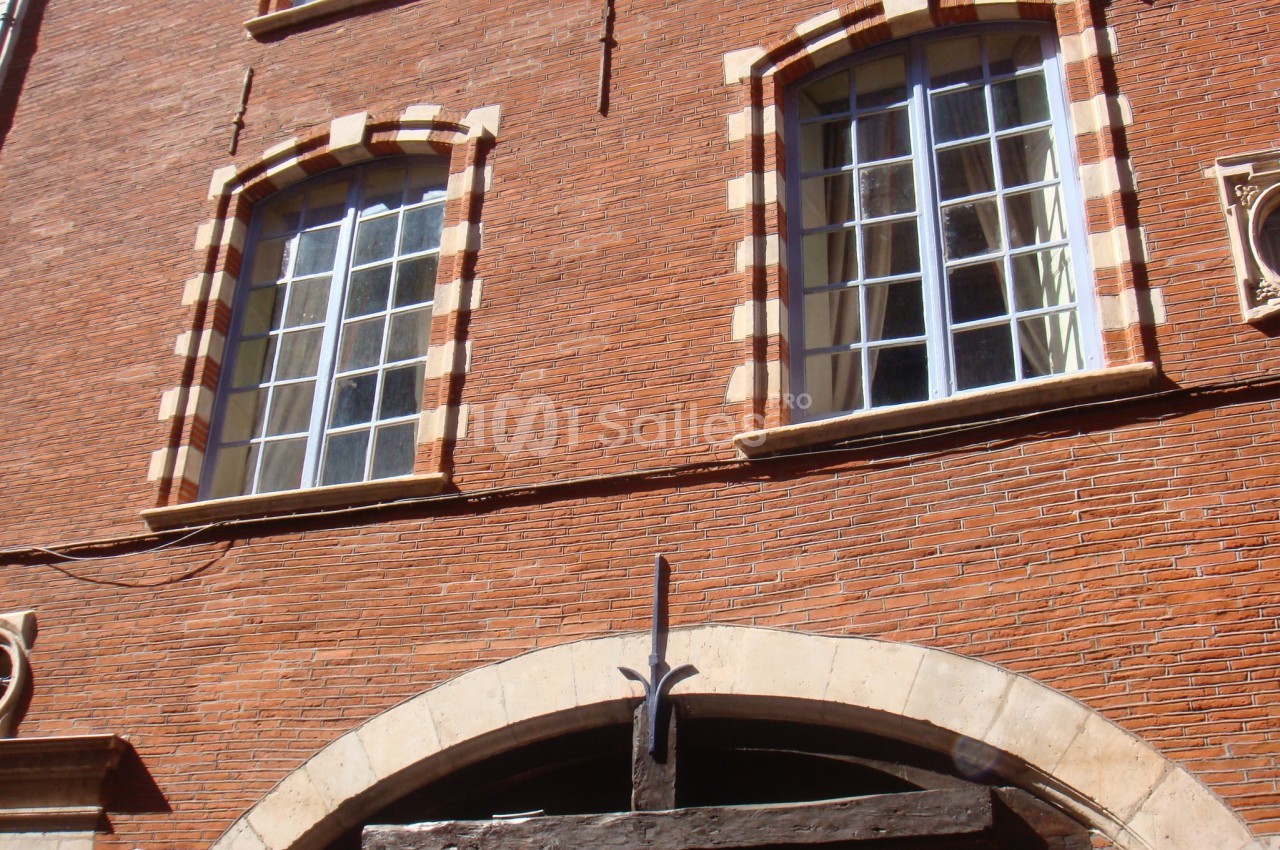 Façade en briques rouges avec fenêtres à encadrement clair et arche en pierre au rez-de-chaussée.