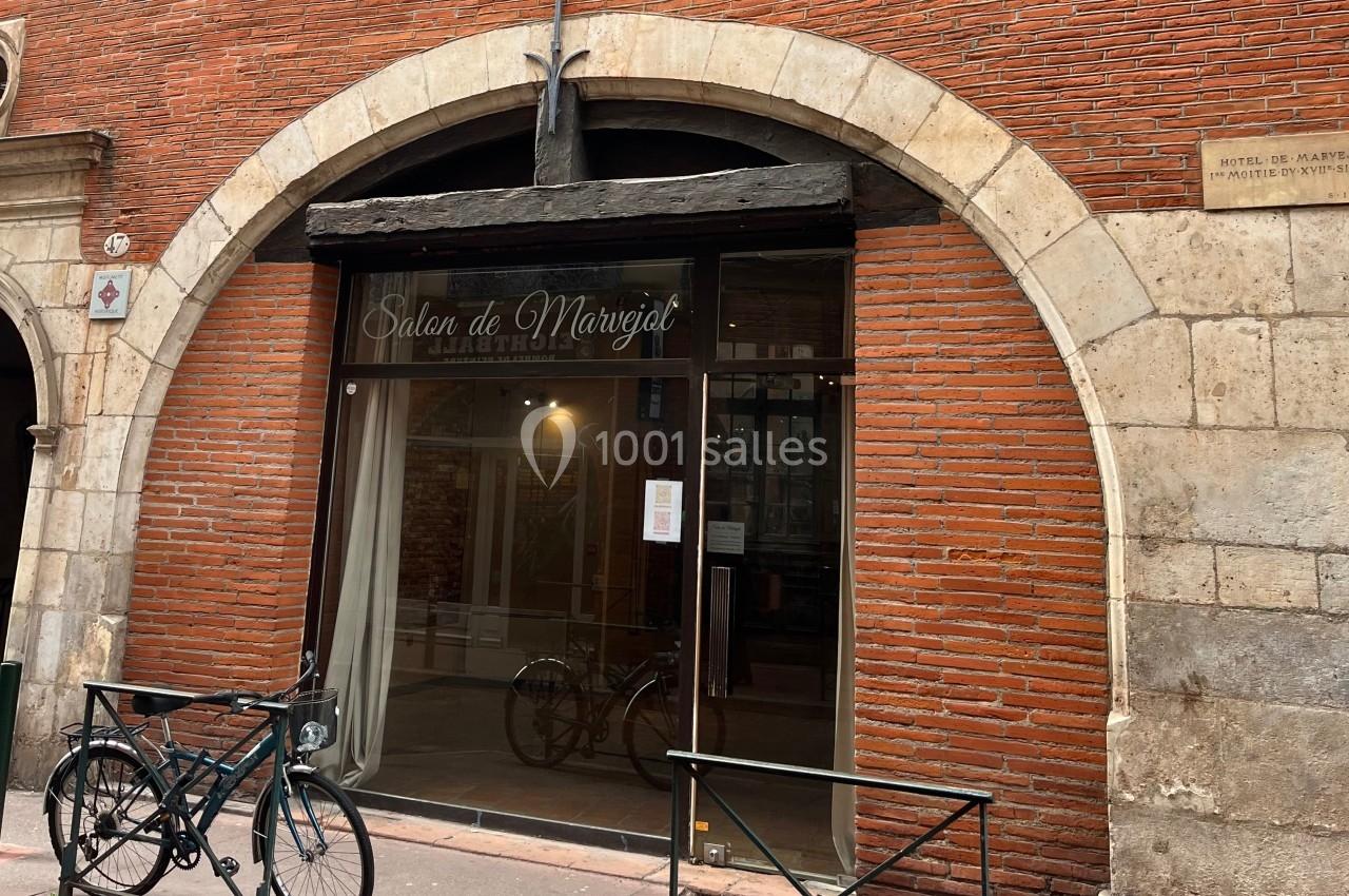 Façade en briques rouges d'un salon avec une grande vitrine et une arche en pierre, deux vélos stationnés devant.