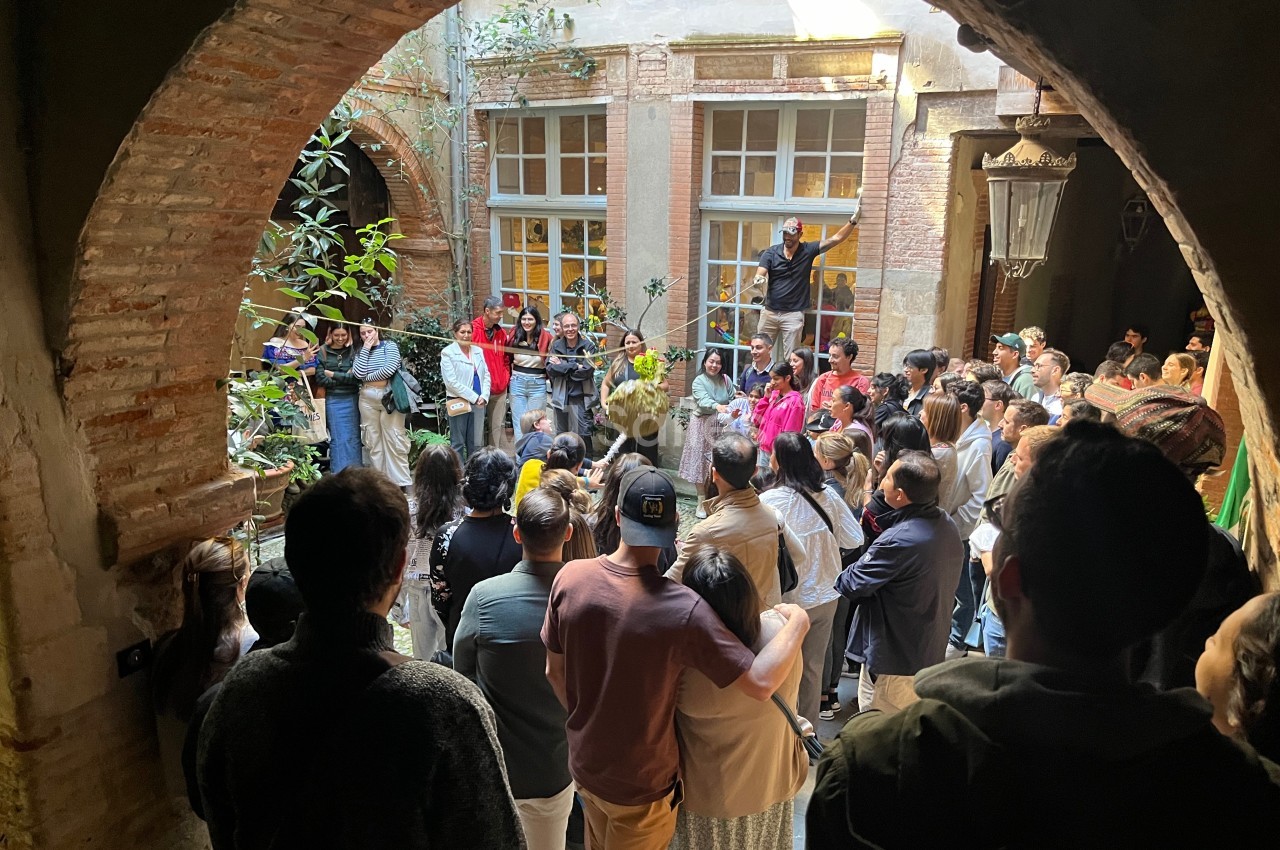 Un groupe de personnes rassemblées dans une cour intérieure, observant une scène sous une arche en briques.