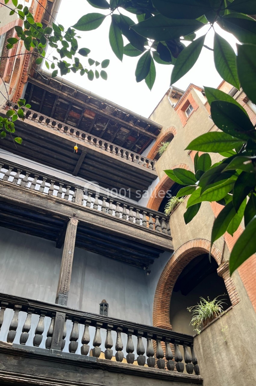 Façade intérieure d'un bâtiment ancien avec balcons en bois sculpté, vue depuis un jardin avec des feuillages au premier…