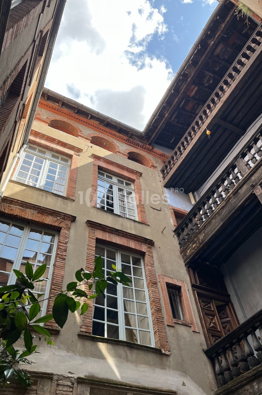 Cour intérieure d'un bâtiment ancien avec façades en briques, balcons en bois et ciel partiellement nuageux.