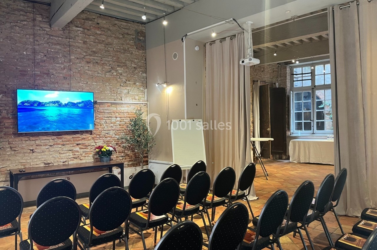 Salle de réunion avec chaises alignées, écran mural, tableau blanc et murs en briques apparentes.