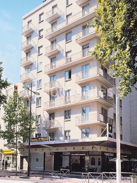 Façade d'un immeuble moderne abritant un hôtel, entouré d'arbres et situé le long d'une rue urbaine.