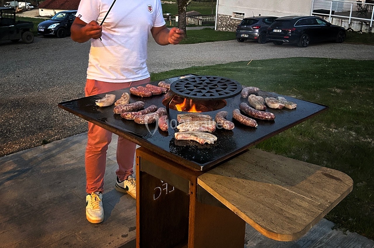 Un homme fait griller des saucisses et de la viande sur un barbecue en plein air, en début de soirée.