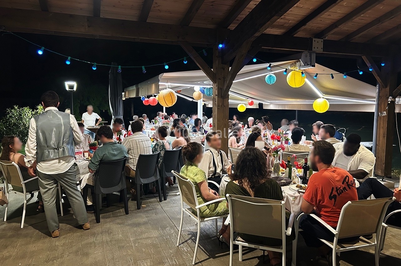 Groupe de personnes dînant sous une pergola éclairée, décorée de lanternes colorées, en soirée.