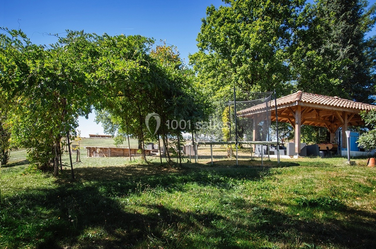 Pergola en bois avec toit en tuiles, entourée de verdure et d'arbres, dans un jardin ensoleillé.