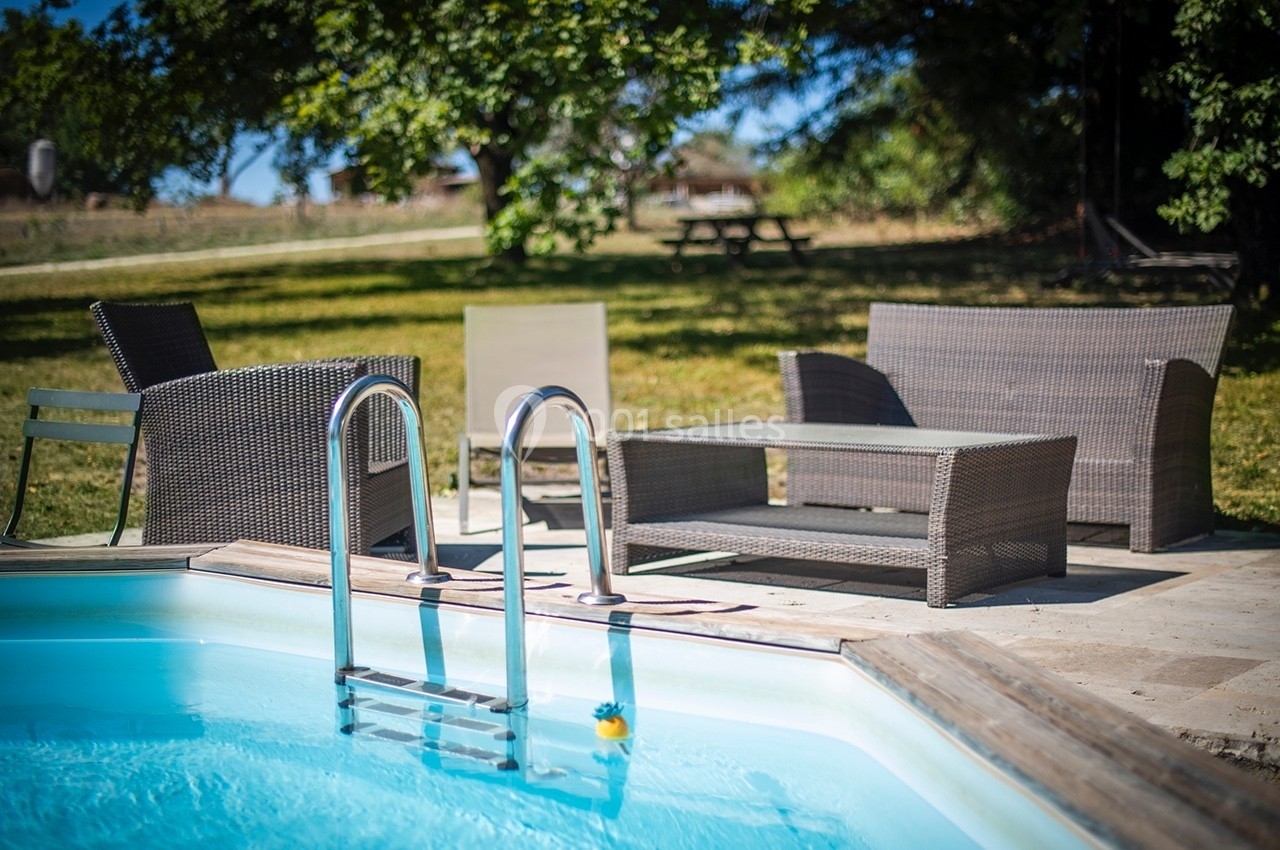 Mobilier de jardin en rotin près d'une piscine, entouré d'herbe et d'arbres sous un ciel dégagé.