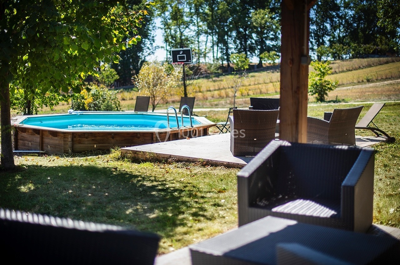 Piscine hors-sol entourée de chaises et fauteuils en plein air, avec un panier de basket en arrière-plan.