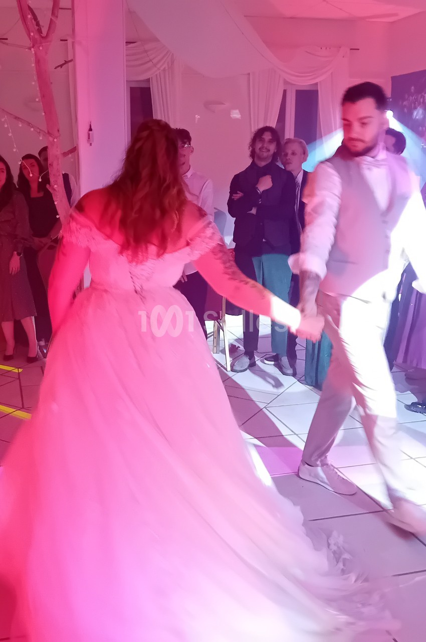 Salle intérieure éclairée en rose vif avec convives dansant sur piste, draperies blanches et ambiance festive.