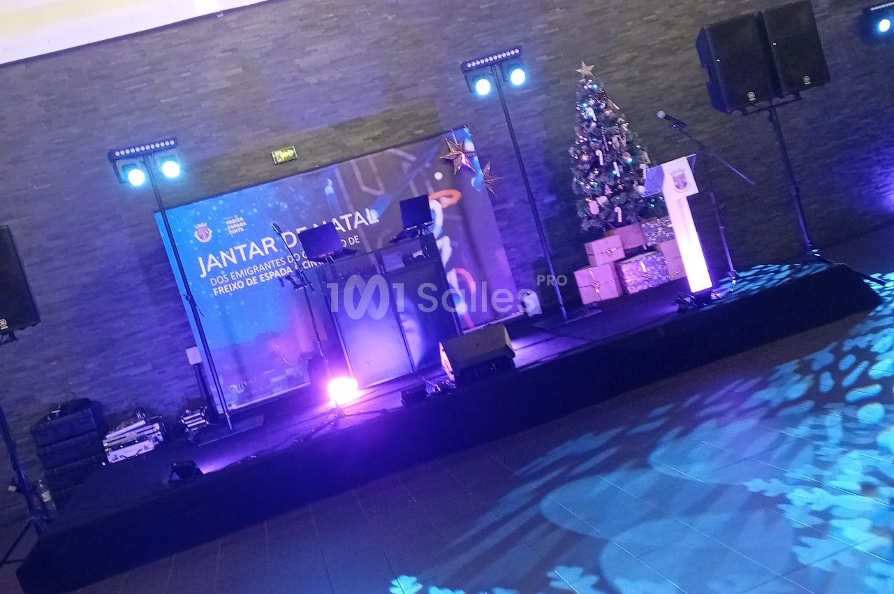 Scène dressée avec podium, écrans, projecteurs bleus et sapin de Noël pour événement festif.