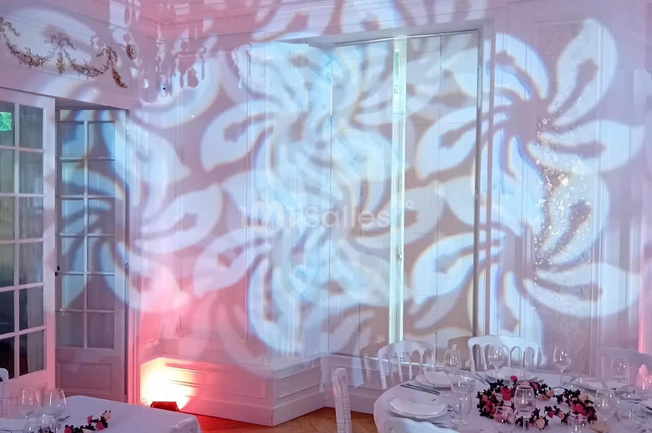 Salle dressée pour banquet avec éclairage rose, projection de motifs floraux et tables de convives.