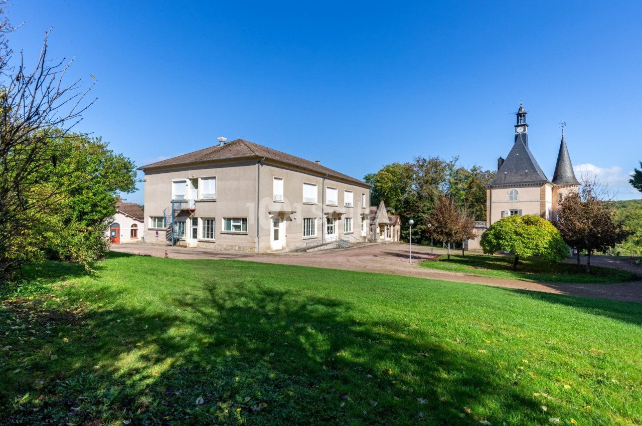 Bâtiment principal beige avec château aux tours pointues en arrière-plan, pelouse verte au premier plan, par temps ensoleillé.