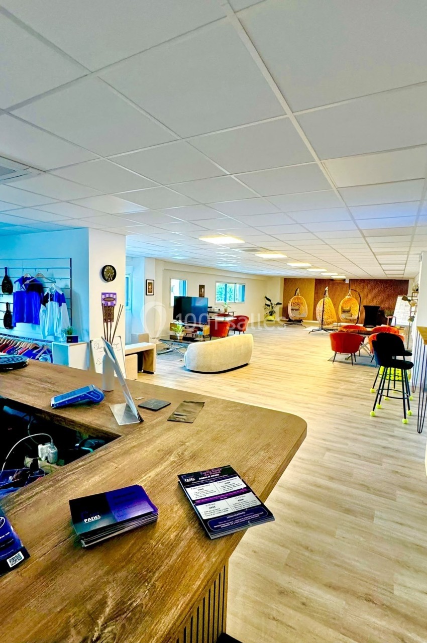 Espace intérieur lumineux avec comptoir en bois, coin salon, fauteuils suspendus et présentoirs de vêtements.