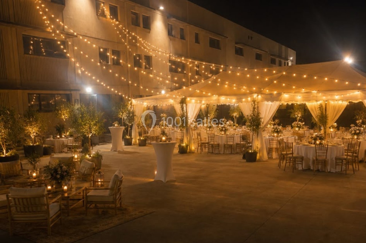 Cour extérieure décorée pour un événement nocturne avec guirlandes lumineuses, tables dressées et tentes éclairées.