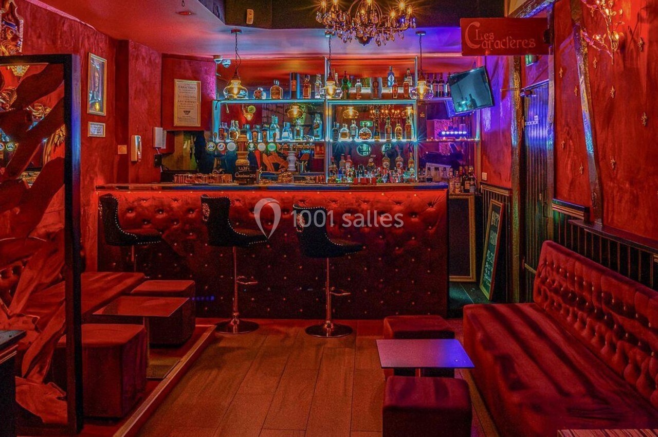 Bar à l'ambiance feutrée avec banquettes rouges, comptoir éclairé et étagères remplies de bouteilles.