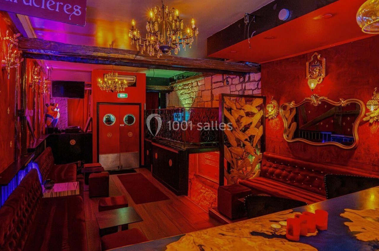 Intérieur d'un bar à l'ambiance chaleureuse avec murs rouges, lustres, banquettes et décorations élégantes.