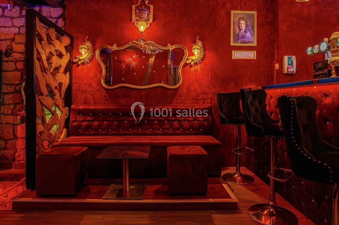 Salon d'un bar à l'ambiance chaleureuse avec canapé rouge, miroir décoratif et comptoir éclairé.