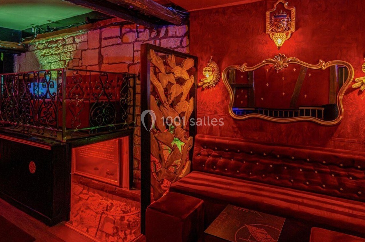 Intérieur d'un bar ou salon avec murs rouges, banquette capitonnée, miroir doré et éclairage tamisé.