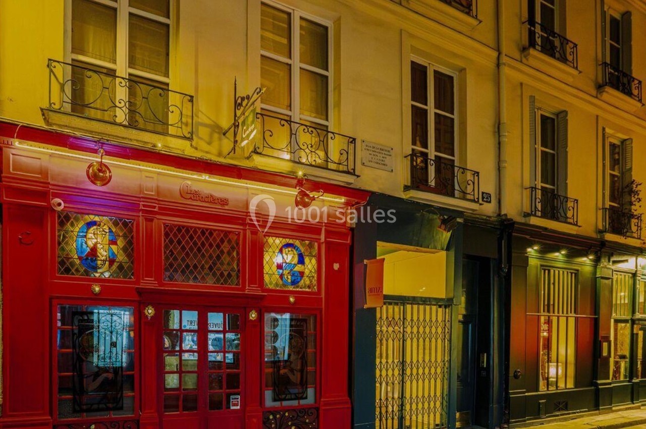 Façade de bâtiments colorés avec une devanture rouge ornée de vitraux, éclairée par des lumières nocturnes.