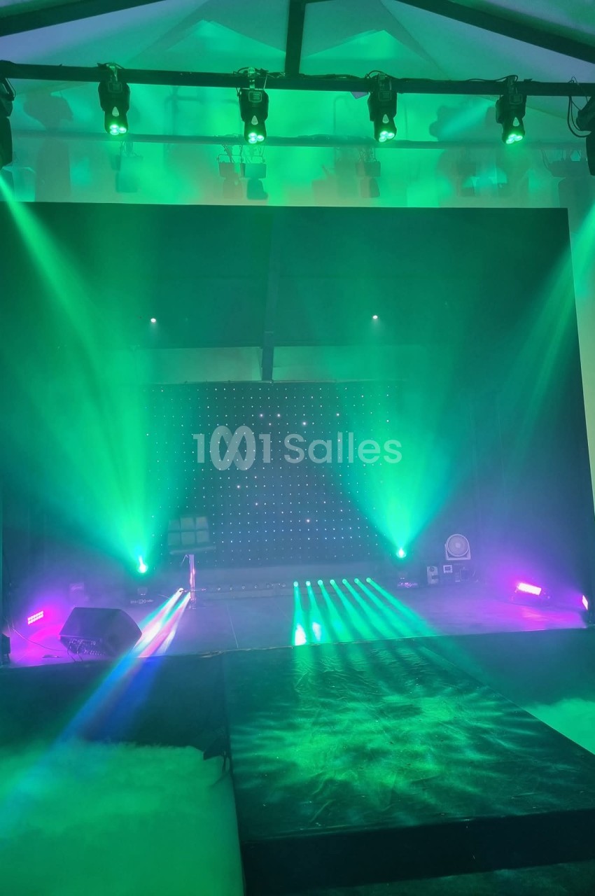 Salle équipée d'une scène, projecteur et projecteurs colorés verts et violets créant une ambiance événementielle.